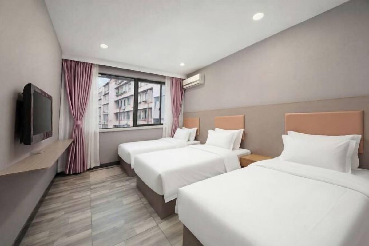 Habitación de hotel con dos camas, televisión, ventana con cortinas y un equipo de aire acondicionado.
