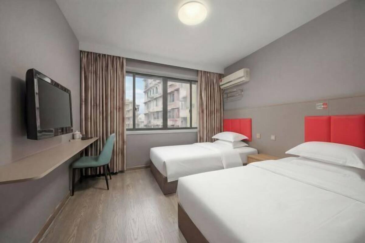 Habitación de hotel con dos camas, televisión, escritorio y ventana con cortinas.