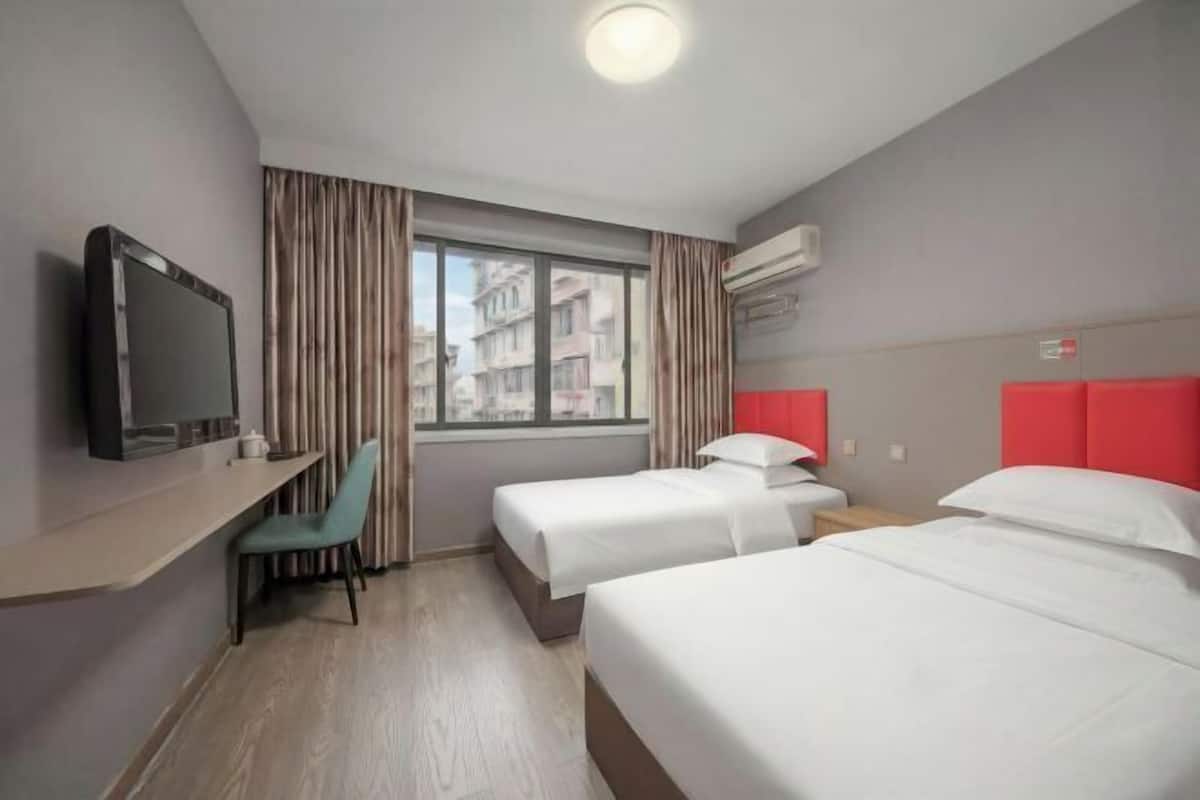Habitación de hotel con dos camas, televisión, escritorio y ventana con cortinas.