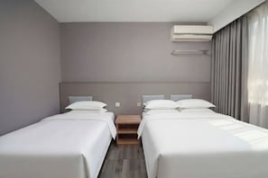 Une chambre d’hôtel avec deux lits, une table de chevet en bois, un climatiseur fixé au mur et une fenêtre avec des rideaux.