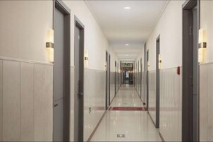 Pasillo de hotel con puertas a ambos lados, una alfombra roja y letreros de salida de emergencia.