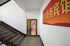A hallway with a staircase, a door with a red sign, and a large red and yellow sign on the wall.