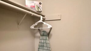 A closet with a hanging rack, a whiteboard, and a box on the wall.