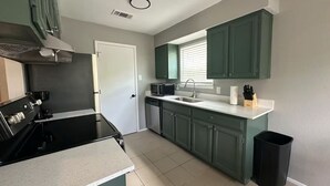 A kitchen with green cabinets, a black stove, a sink, and a trash can.
