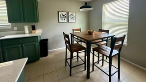 A kitchen with green cabinets, a wooden dining table, and two framed pictures on the wall.