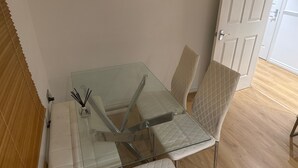 A dining area with a glass table, white cushioned chairs, and a white door in the background. - Stylish Apartment in Chafford Hundred (Grays)