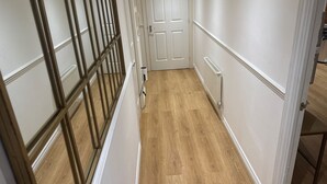 A narrow hallway with wooden flooring, white walls, and a white door at the end. - Stylish Apartment in Chafford Hundred (Grays)