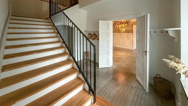 A wooden staircase with black railings leading to a room with white doors and a chandelier. - Nice home in Ekeby with WiFi (Ekeby)