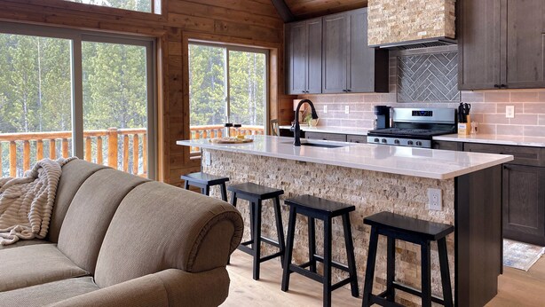 Una cocina moderna con una isla de piedra, armarios oscuros y vistas al bosque.