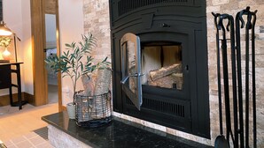 Una chimenea de piedra con marco negro, una planta en maceta y una baranda metálica.