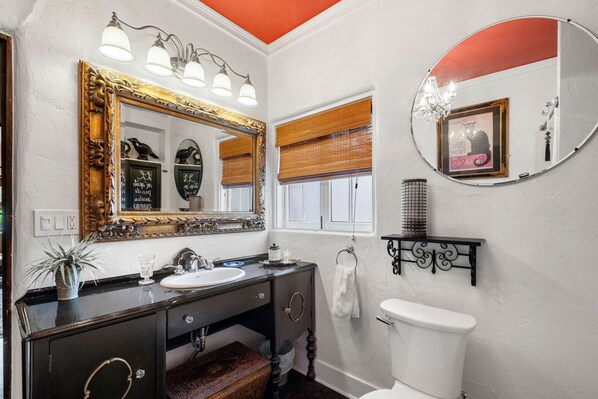 A bathroom with a large ornate mirror, a sink, a toilet, and a window with blinds. - Rock House Haven Retreat (Prescott)