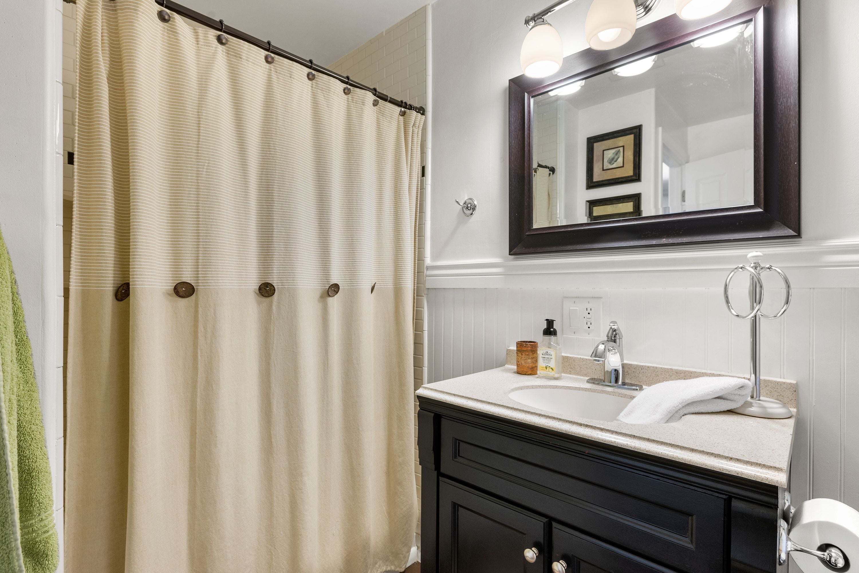 A bathroom with a beige shower curtain, a sink with a mirror above it, and a towel hanging on the wall.