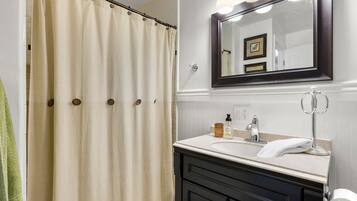 A bathroom with a beige shower curtain, a sink with a mirror above it, and a towel hanging on the wall.