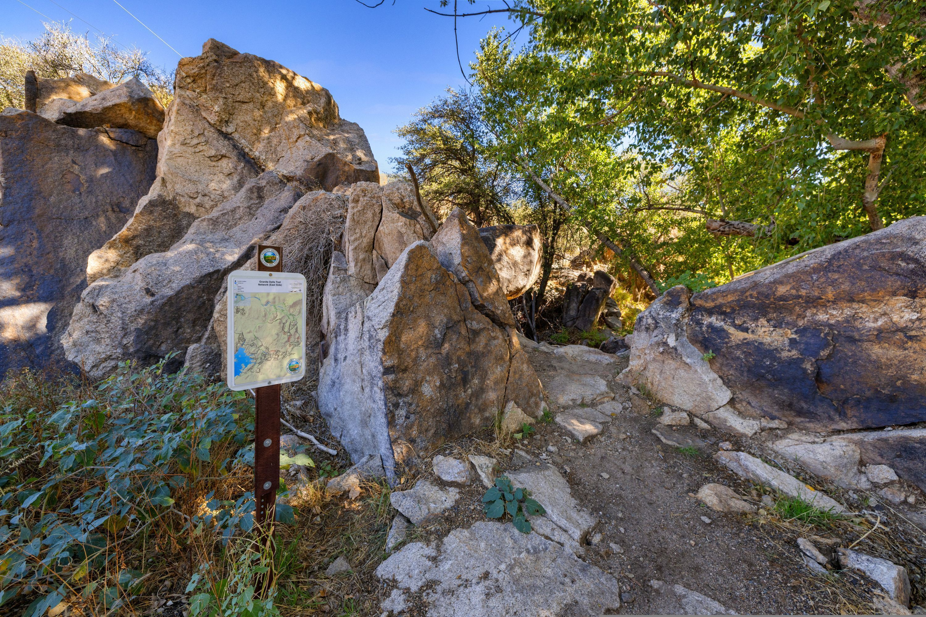 A rocky trail with a signpost, surrounded by trees and vegetation.