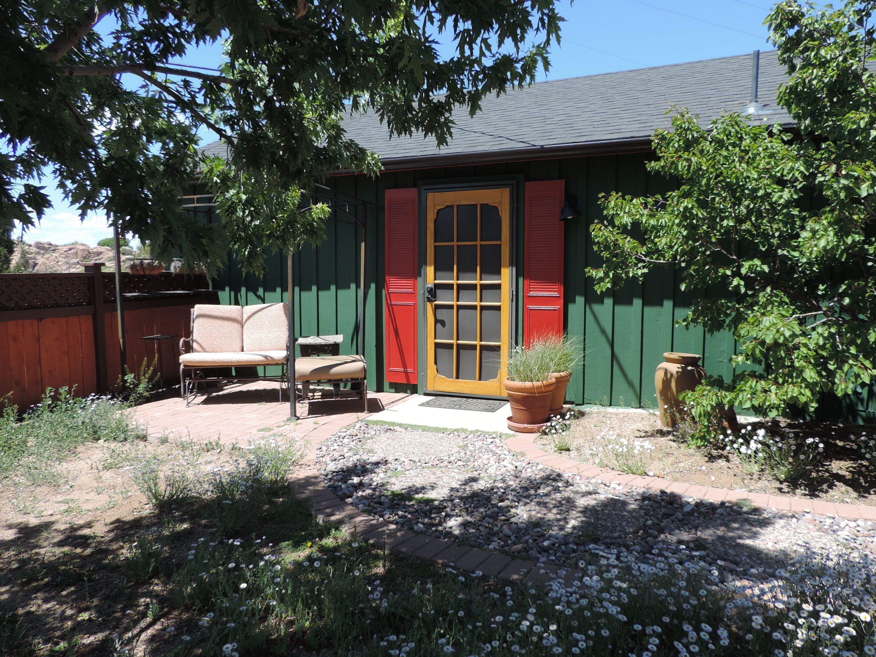 A small house with a green exterior, a red door, and a patio with a chair and table.
