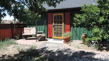 A small house with a green exterior, a red door, and a patio with a chair and table.