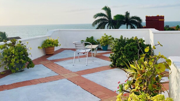 Terraza en la azotea con vistas al mar, que incluye una mesa y sillas blancas, plantas en macetas y una chimenea roja.