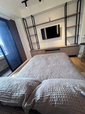 A modern bedroom with a large bed, a flat-screen TV mounted on a wall, and a sliding glass door leading to a balcony. - Comfortable Loft Normandy 605 (Bogotá)