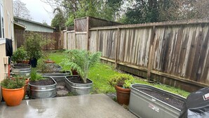 Een betonnen terras met potplanten en een houten omheining op de achtergrond.