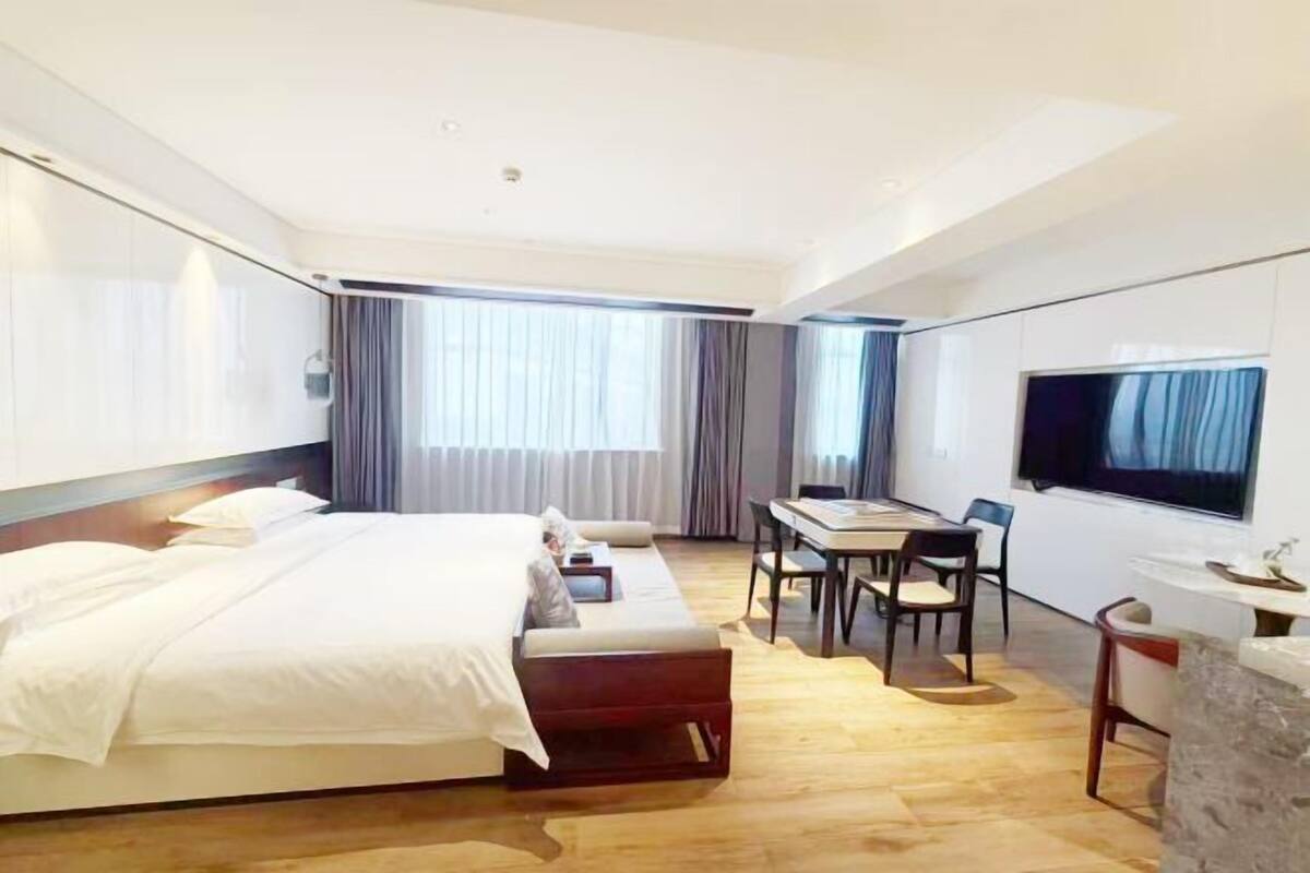 Ein modernes Hotelzimmer mit Bett, Schreibtisch, Fernseher und einem großen Fenster mit Vorhängen.