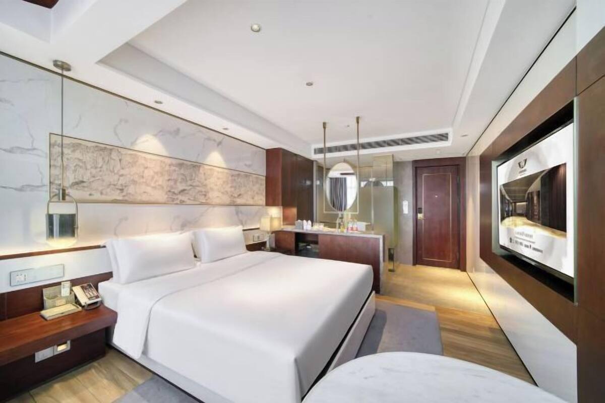 Ein modernes Hotelzimmer mit einem großen Bett, einem Schreibtisch, einem Schminktisch und einem Fernseher.