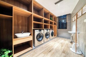 A modern laundry room with wooden shelving, a sink, and two washing machines. - Hongye Youyi Hotel (Yongkang)