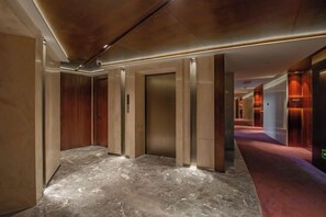 Un pasillo de hotel con ascensores, suelo de mármol y alfombra roja.