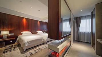 A modern hotel room with a large bed, a flat-screen TV, a fireplace, and a large mirror.