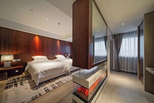Una habitación de hotel moderna con una cama grande, un televisor de pantalla plana, una chimenea y un espejo amplio.