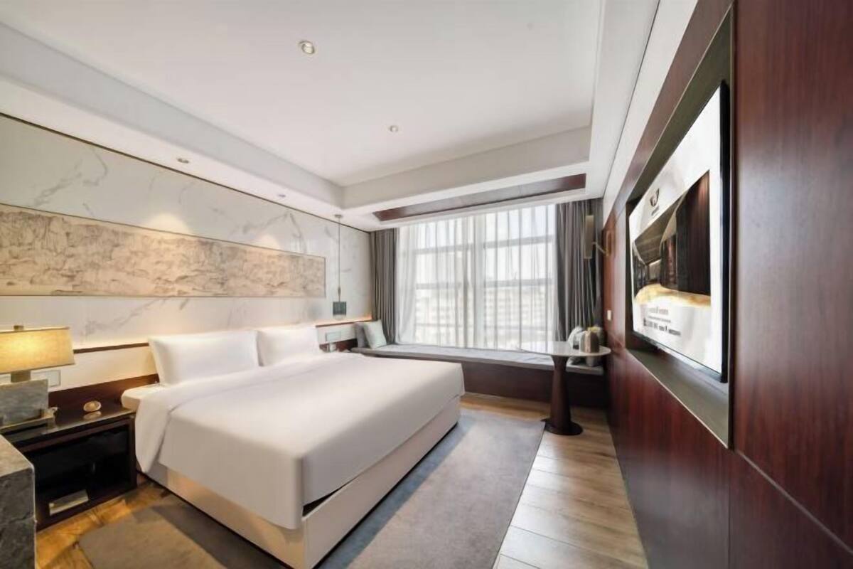 Ein Hotelzimmer mit einem großen Bett, einem an der Wand montierten Fernseher, einem Fenster mit Vorhängen und einer Marmorwand.