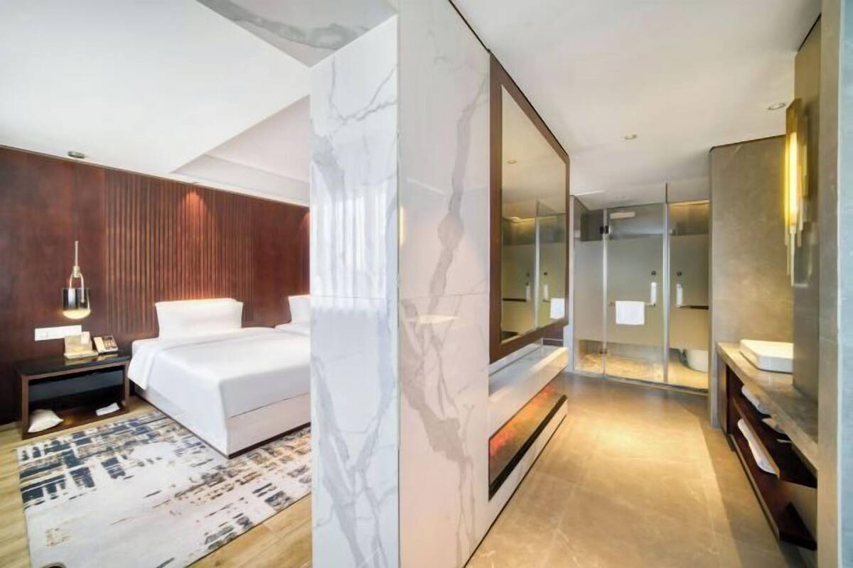 Ein modernes Hotelzimmer mit einem großen Bett, einem Nachttisch, einem Spiegel und einem Badezimmer mit Duschkabine.