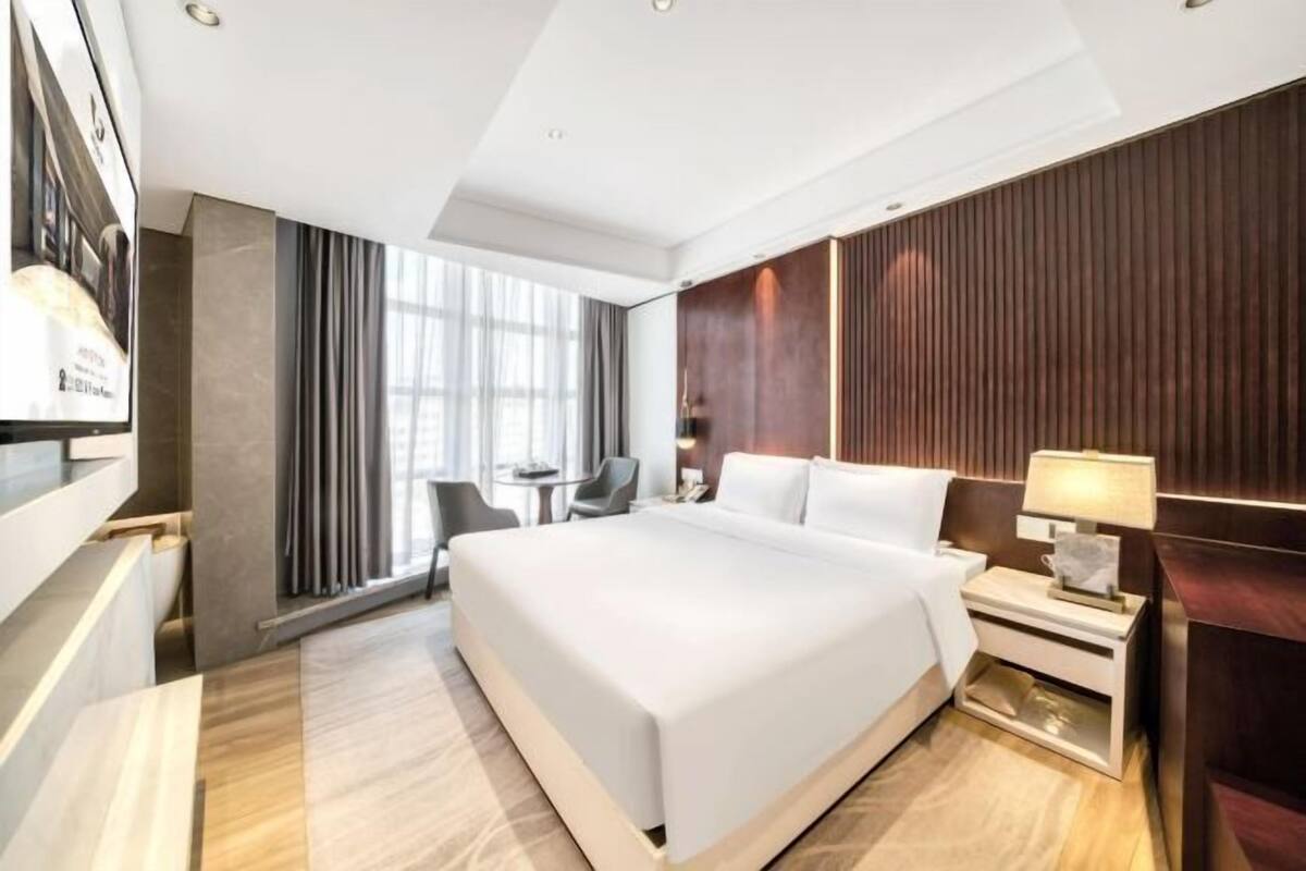 Ein modernes Hotelzimmer mit einem großen Bett, einem Schreibtisch, einem Stuhl und einem Fernseher.