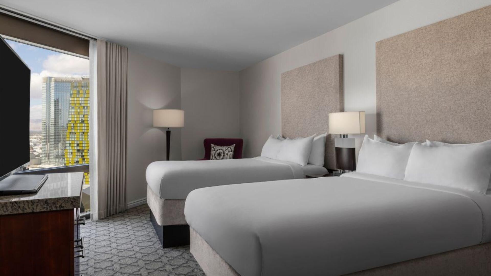 Ein Hotelzimmer mit zwei Betten, einem Schreibtisch und Blick auf die Stadt.
