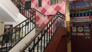 Una escalera con un muro a cuadros rosa y blanco, barandilla de madera y pasamanos metálico.