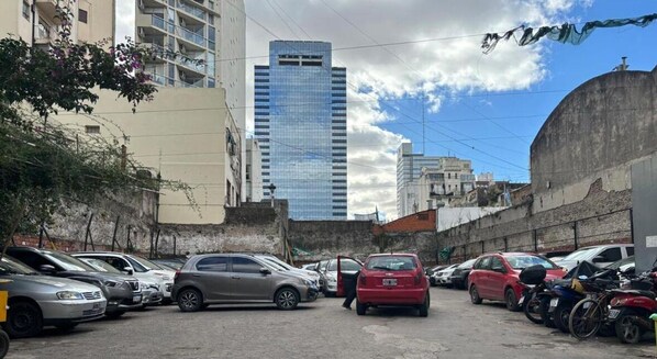 A parking lot with several cars and motorcycles, surrounded by buildings including a tall glass skyscraper. - Hostelmo Hotel & Hostel (Buenos Aires)