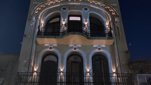 Un edificio histórico con una amplia entrada central, varios balcones con barandillas de hierro forjado y un letrero que indica que es un albergue.