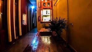 Un estrecho pasillo con un banco de madera y una mesita, que conduce a una habitación con ventana y puerta.