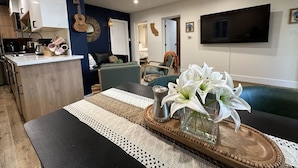 A modern living room with a dining area, a kitchen, and a TV mounted on the wall.