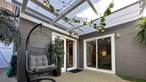 A covered patio with a hanging chair, a wooden table, and a sliding glass door leading to a bedroom.