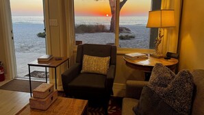 A room with a view of the sunset over the ocean, a sofa, a small table with a lamp, and a decorative mirror.