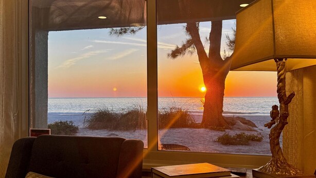 A room with a large window offering a view of the sunset over the ocean, a lamp, and a statue on a table.
