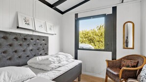 A bedroom with a bed, a chair, a mirror, and a window with a view of greenery.