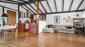 A spacious living area with a wooden floor, a kitchen with modern appliances, and a dining area with metal chairs.