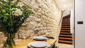 Una mesa de comedor servida con platos, cubiertos y un florero frente a una pared con textura.