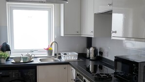 A modern kitchen with white cabinets, a built-in washing machine, a microwave, and a sink.