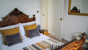 A neatly made bed with a striped bedspread and multiple pillows, a wooden headboard, a bedside table with a lamp, and a door with a mirror.