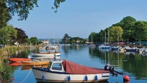 A calm water body with several boats docked, surrounded by trees and a clear sky.