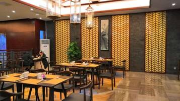A restaurant with tables and chairs, a large plant, and a herringbone-patterned wall.