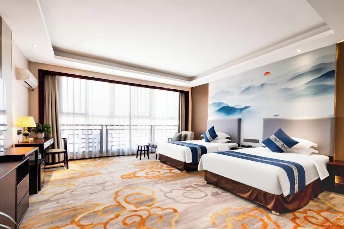 A hotel room with two beds, a desk, a chair, a large window, and a mural on the wall.