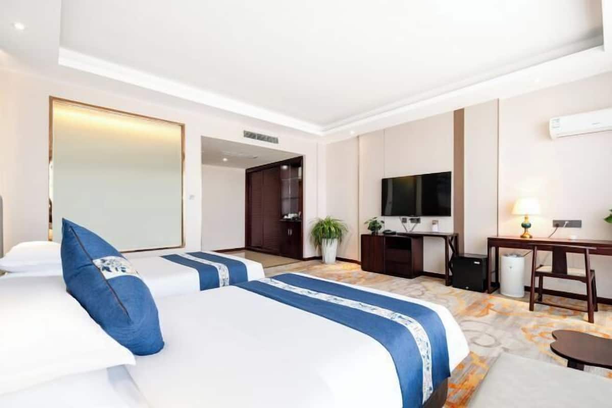 A hotel room with two beds, a desk, a TV, and a bathroom.